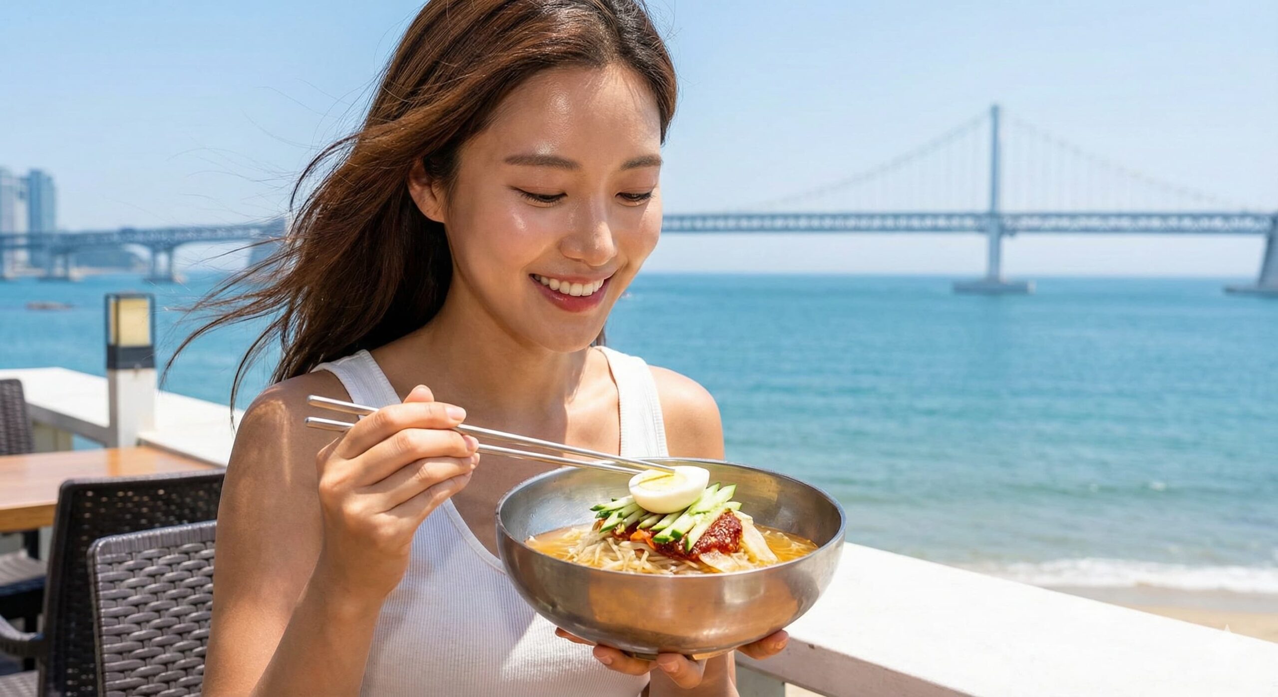 광안대교가 보이는 해변 테라스에서 부산 로컬 미식인 밀 면을 먹으며 워케이션의 여유를 즐기는 여성 모델